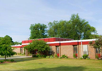 Exterior of a single story brick school with sign out front