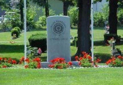 I single large headstone with flowers and green grass in front of it.