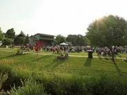 green field in summer crowded with people outside a bandshell