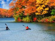 Two people kayaking on the lake with fall foliage in the background