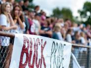 A banner with the words Buck Pride hanging on a fence with fans on the bleachers in the background