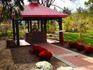 A red roofed structure housing historic firehouse bell with red and white flowers