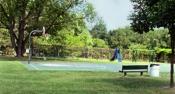 Basketball court surrounded by trees and a green bench