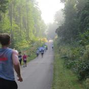Marathon runners on a paved path through a green, wooded trail