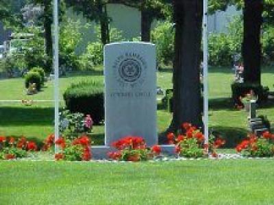 I single large headstone with flowers and green grass in front of it.